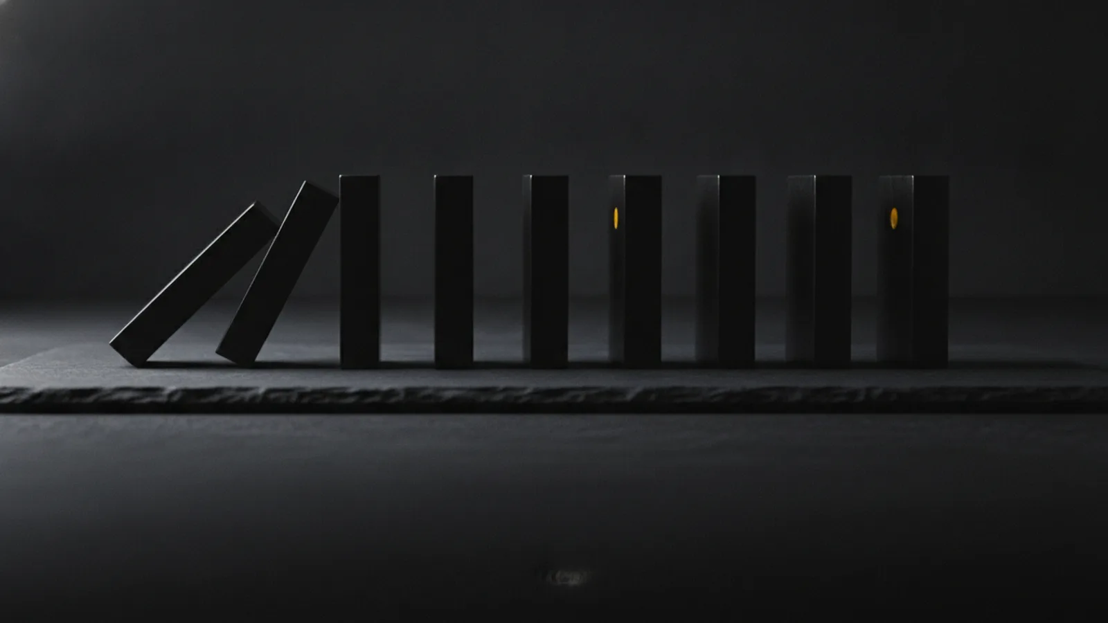 Une rangée de dominos noirs dressés sur une table sombre, le premier domino basculé vers l’avant en pleine chute.