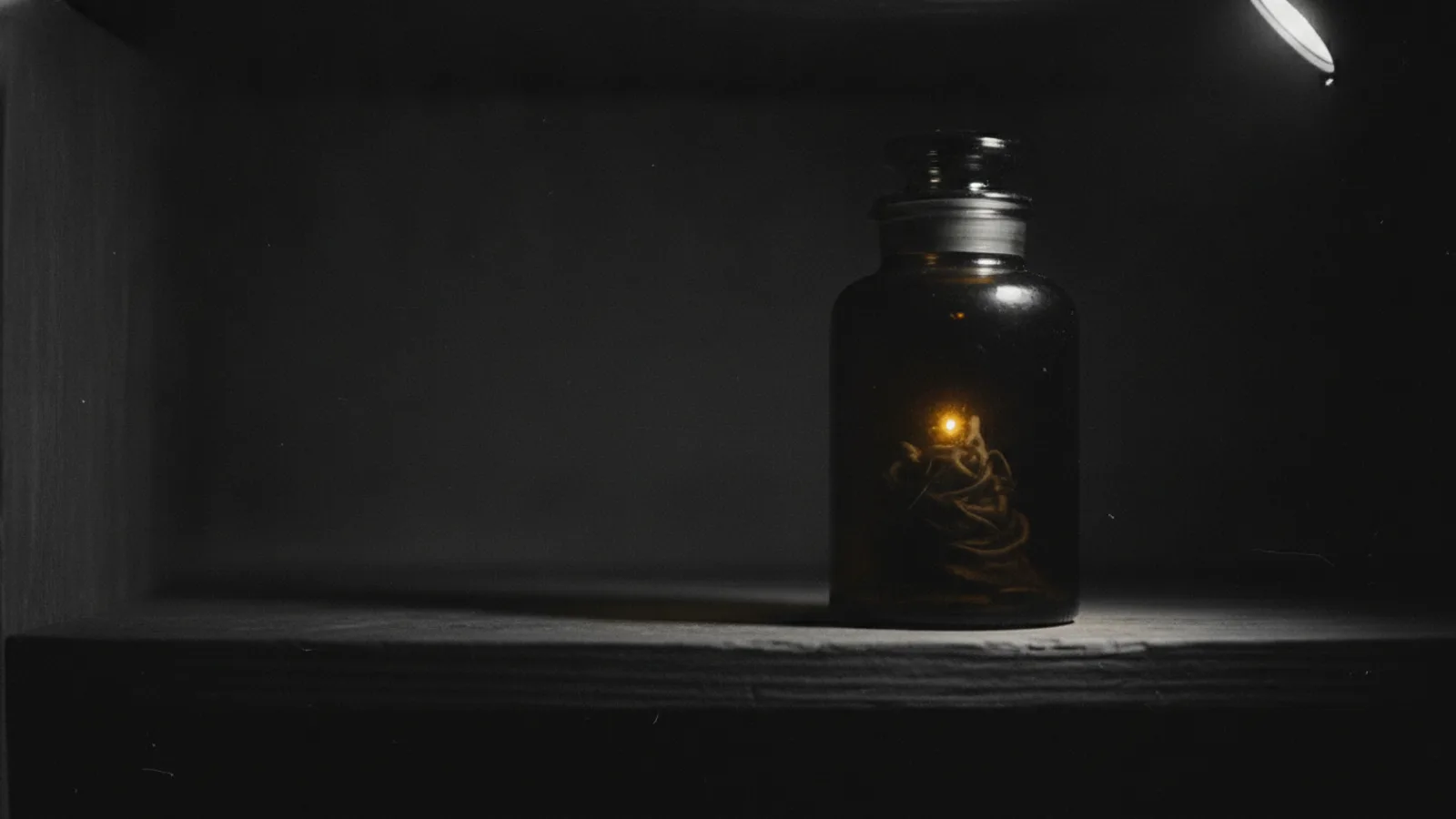 Un bocal de verre sombre scellé posé sur une étagère, une seule LED ambre allumée à l’intérieur, le reste du contenu invisible pour le scanner.