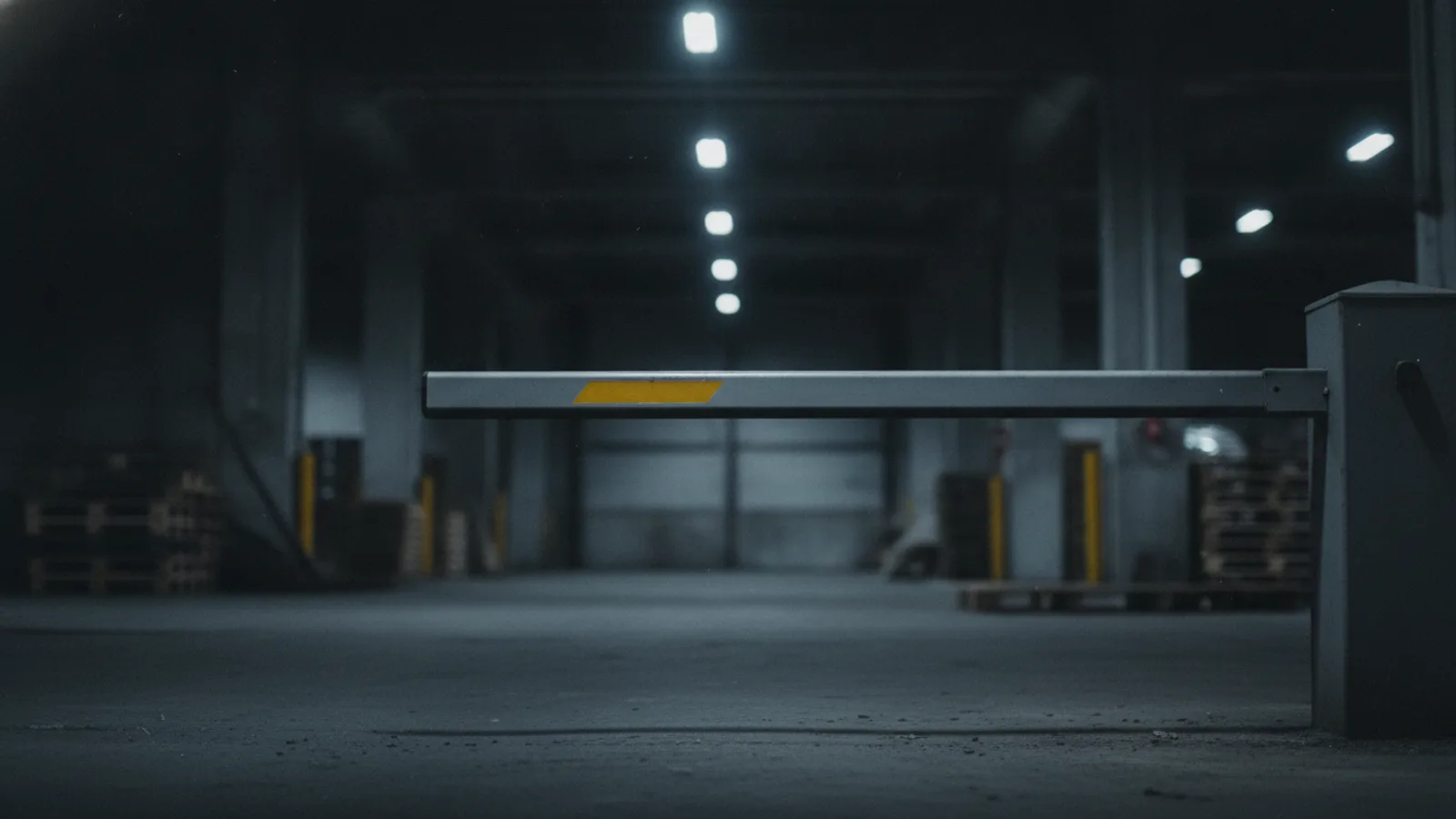 A metal barrier arm held down across an empty warehouse loading dock, a single amber-yellow stripe on the arm.