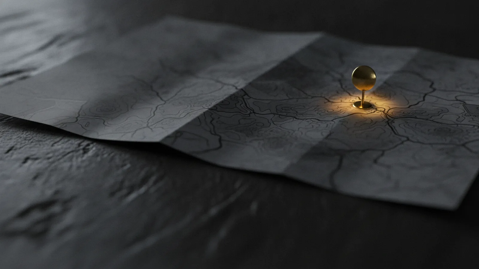Une carte routière en papier dépliée sur une table, un seul repère à punaise planté sur un point.
