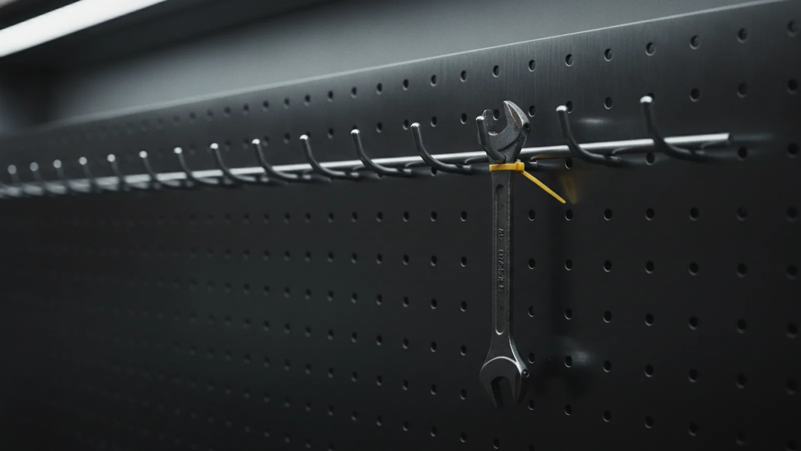 A steel pegboard where several worn tools have been removed leaving clean empty hooks, one remaining tool tagged with a single amber cable tie.