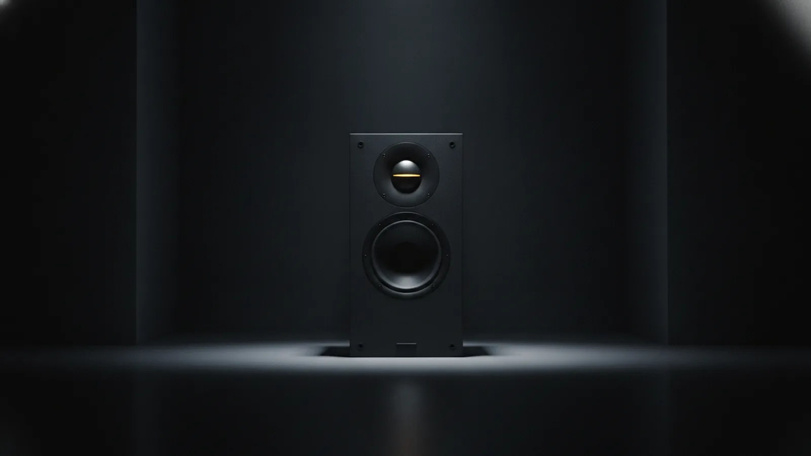 A matte-black bookshelf speaker in a dark room, its amber tweeter dome catching a thin highlight.
